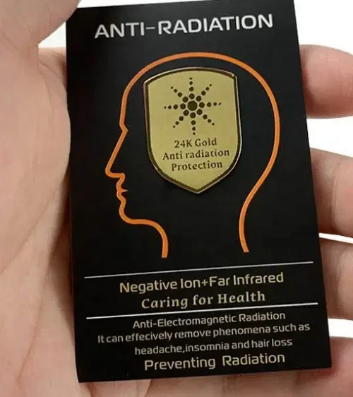 A hand is holding a black card that says ANTI-RADIATION. The card has a gold badge on it that reads 24K Gold Anti-Radiation Protection. The card says it can protect you from radiation and lists health benefits, as well as ways to prevent different symptoms.