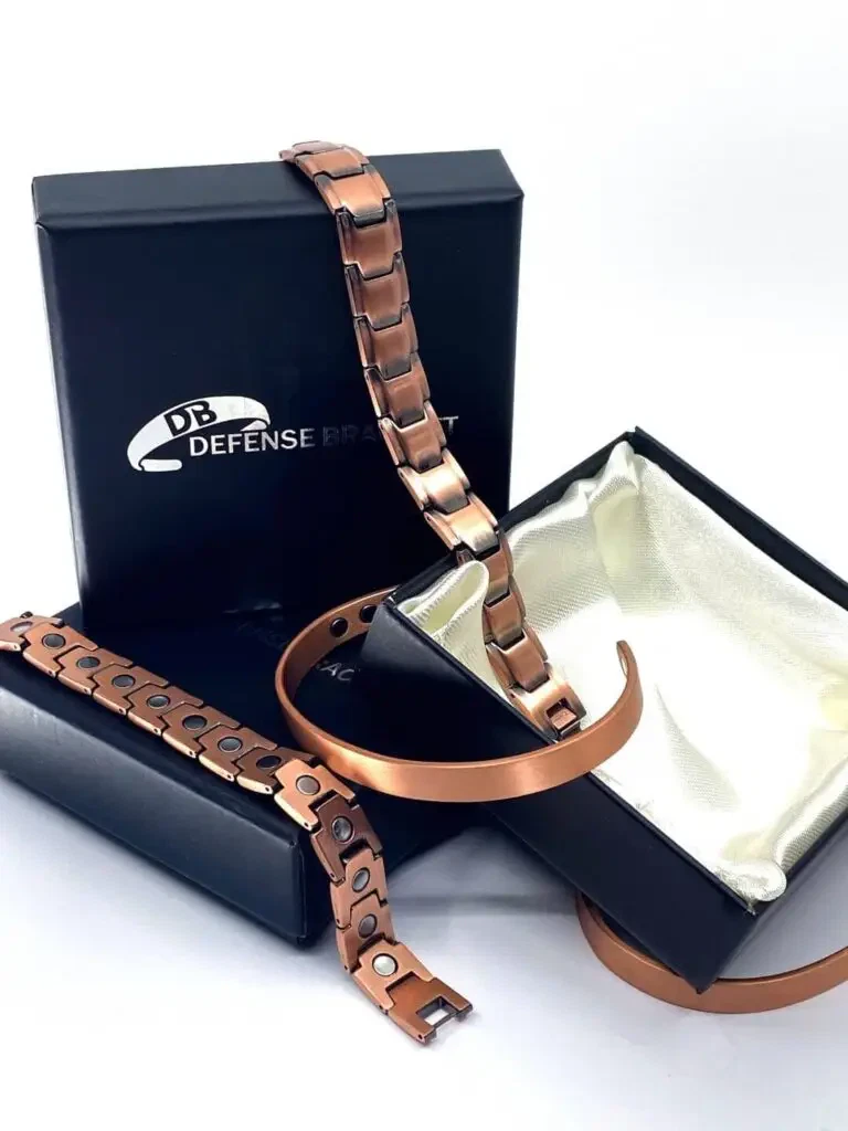 Copper-colored metal bracelets sit on and around black boxes that say Defense Bracelet. One box is open and has a satin-lined inside.