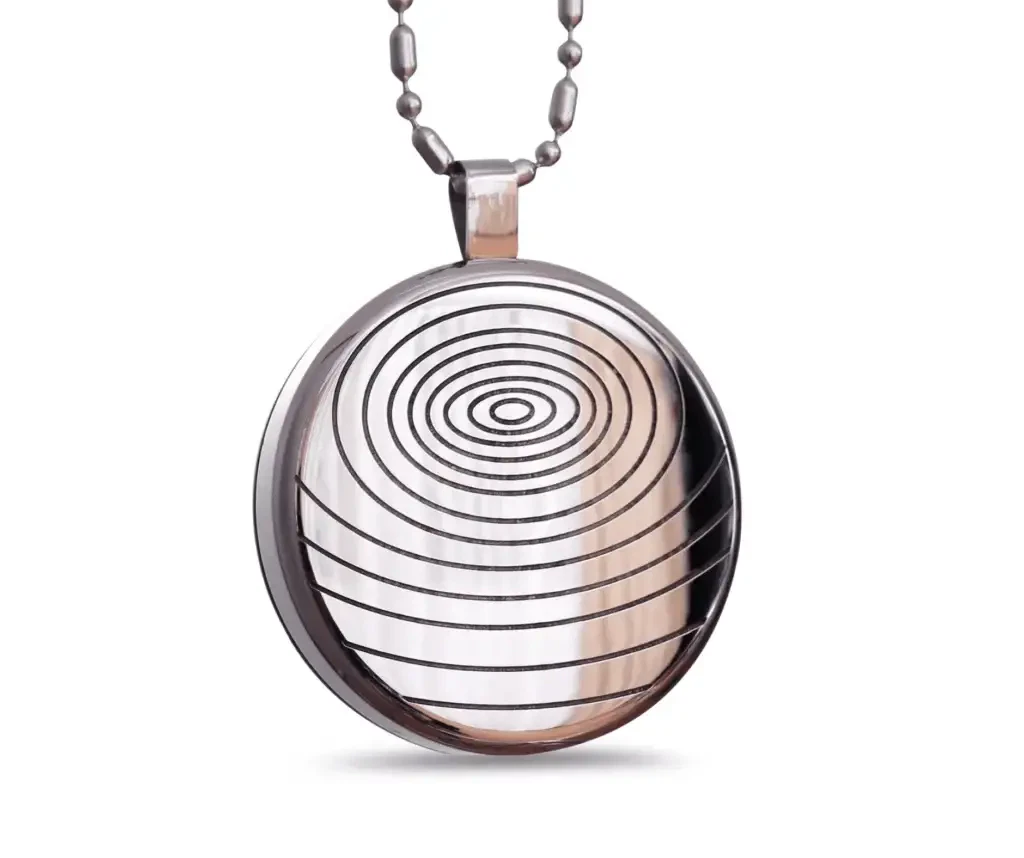 A shiny, silver oval pendant with engraved circles hangs on a metal chain. The surface of the pendant is so reflective that you can see rings carved into it, making it look like a swirling spiral.