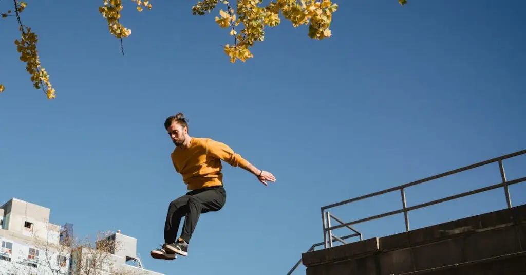Someone wearing a yellow sweater and black pants is jumping in the air against a clear blue sky. Theyre close to a concrete building, with some yellow leaves peeking at the top. City buildings can be seen in the background.