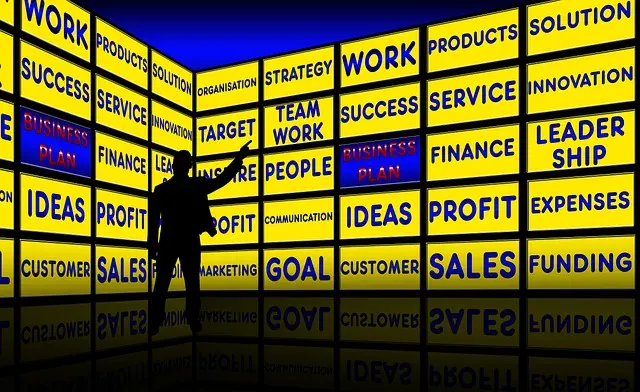 A shadowy figure is pointing at a wall filled with yellow and blue screens. These screens show business words like TARGET, TEAM WORK, and GOAL SETTING. These words are about planning, growing personally, and achieving success.